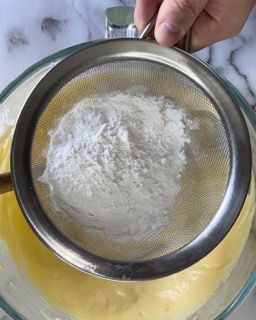 Una persona sta setacciando la farina in una ciotola piena di liquido.