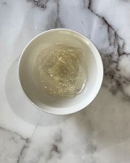 Una ciotola bianca piena di liquido trasparente è appoggiata su una superficie di marmo.