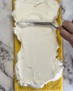 Una persona sta spalmando la panna montata su una torta gialla con una forchetta.