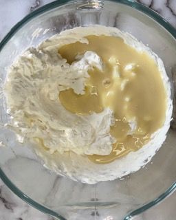 Una ciotola di vetro piena di panna montata e un liquido giallo.