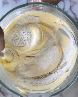 Una persona sta mescolando un impasto in una ciotola di vetro con un cucchiaio.