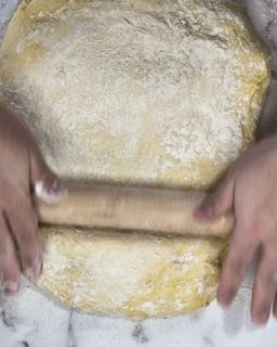 Una persona sta stendendo la pasta con un mattarello di legno.