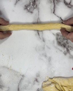 Una persona sta stendendo un pezzo di pasta su una superficie di marmo.