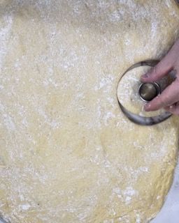 Una persona sta usando uno stampino per ciambelle per ricavarne una dall'impasto.
