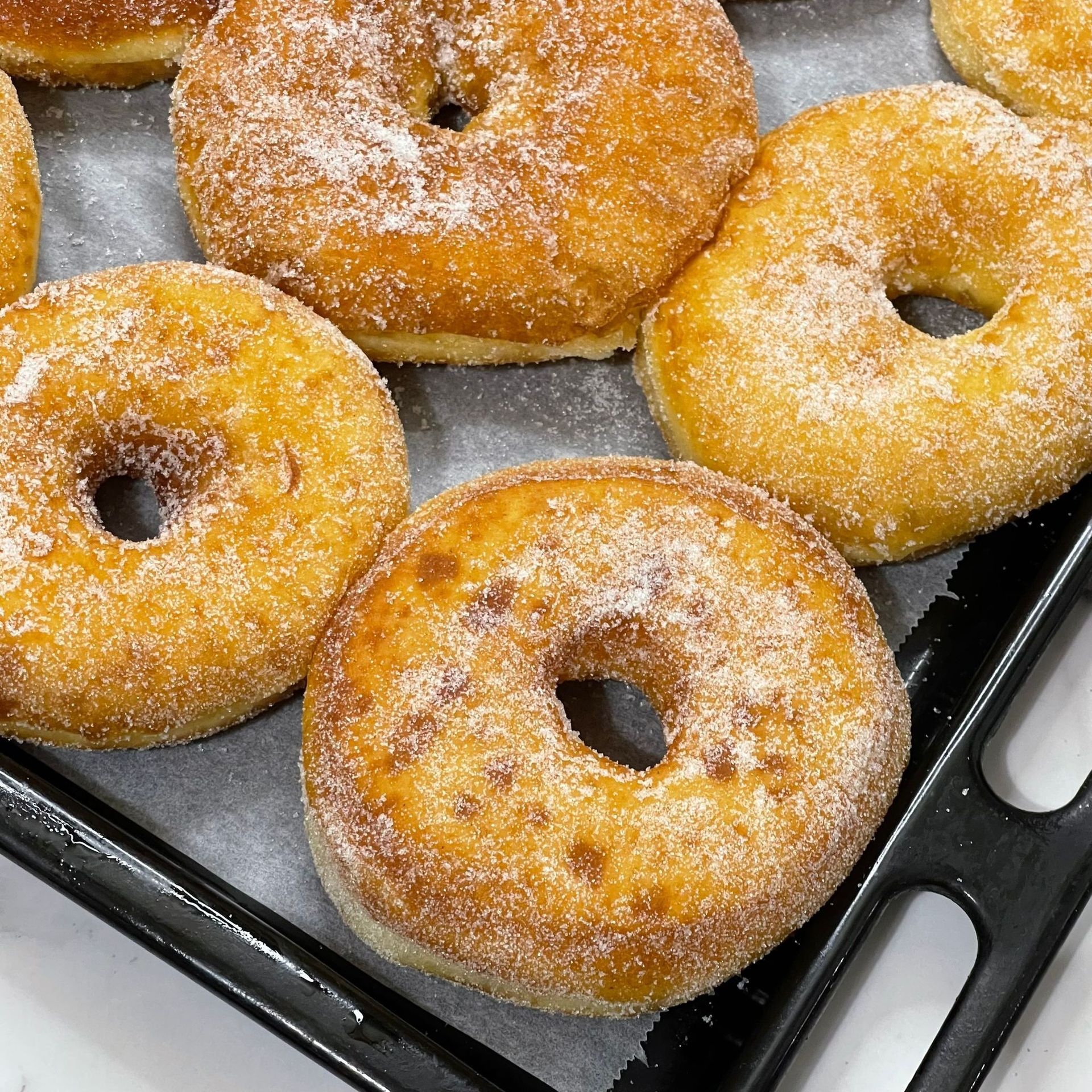 Un mucchio di ciambelle ricoperte di zucchero a velo su una padella.