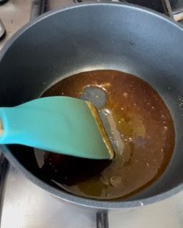 Una spatola blu sta mescolando un liquido marrone in una padella