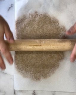 Una persona sta stendendo un pezzo di pasta con un mattarello di legno.