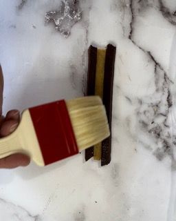 Una persona tiene in mano un pennello sopra un pezzo di cioccolato.