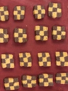 Un mucchio di biscotti a scacchi marroni e gialli su un panno rosso.