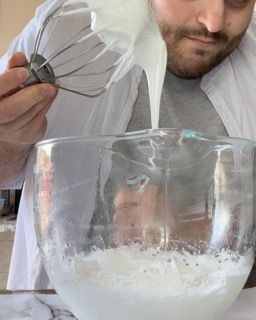 Un uomo sta versando la panna montata in una ciotola di vetro.
