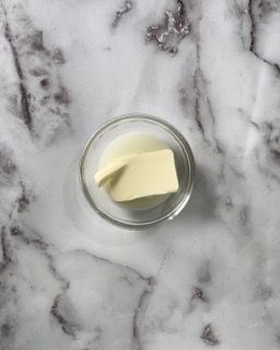 Un pezzo di burro si trova in una piccola ciotola di vetro su una superficie di marmo.