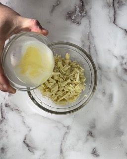 Una persona sta versando del burro in una ciotola di formaggio grattugiato.