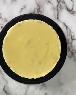Una cheesecake gialla su un piatto nero su una superficie di marmo