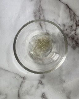 Una ciotola di vetro piena di liquido è appoggiata su una superficie di marmo.