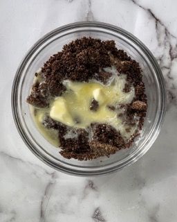 Una ciotola di vetro piena di briciole di cioccolato e burro fuso.