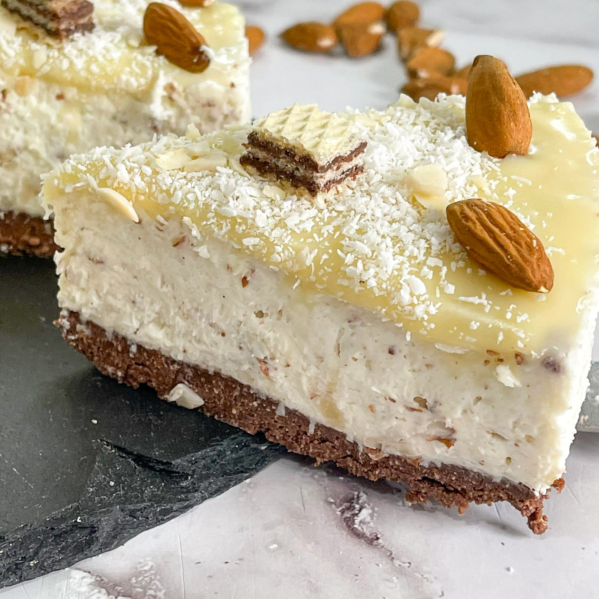 Una fetta di cheesecake con mandorle e cocco sopra.
