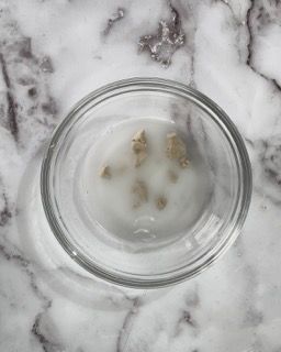 Una ciotola di vetro piena di un liquido bianco è appoggiata su una superficie di marmo.