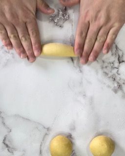 Una persona tiene in mano un pezzo di pasta su un tavolo.