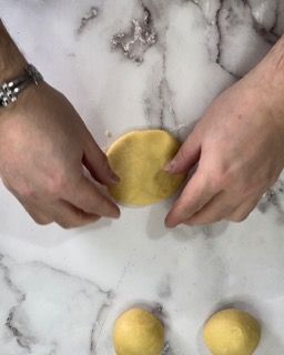 Una persona tiene in mano un pezzo di pasta su un tavolo.