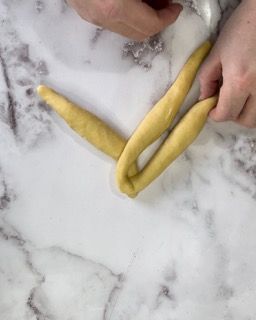 Una persona tiene in mano un pezzo di pasta su una superficie di marmo.