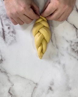 Una persona sta intrecciando un pezzo di pasta su una superficie di marmo.