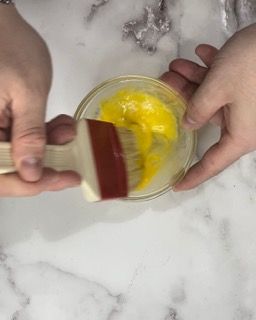 Una persona tiene un pennello sopra una ciotola piena di liquido giallo.