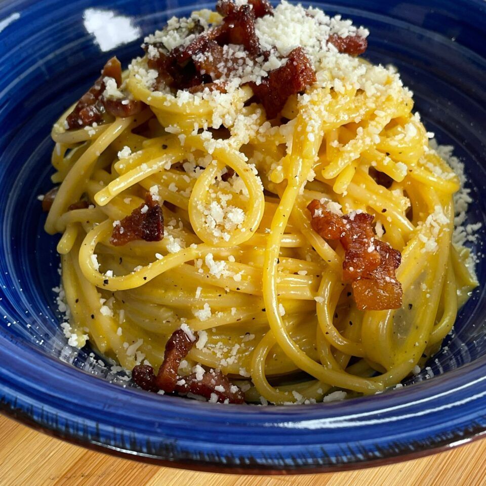 Una ciotola blu piena di spaghetti e formaggio su un tavolo di legno.