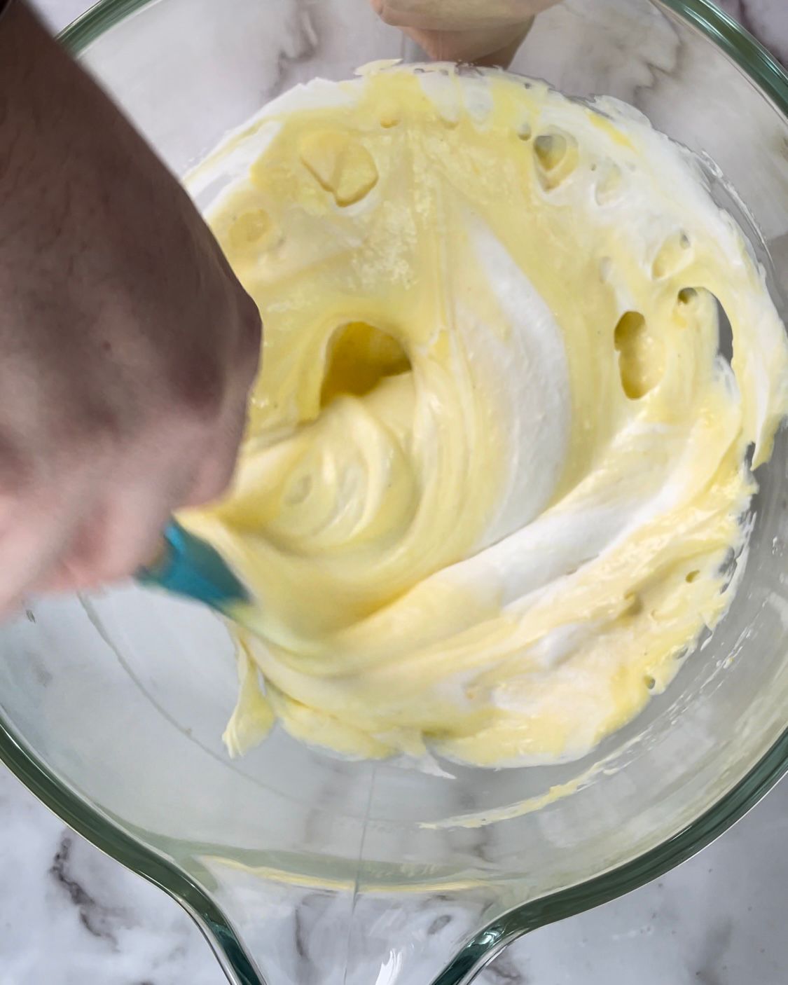 Una persona sta mescolando un liquido giallo in una ciotola di vetro con una spatola.