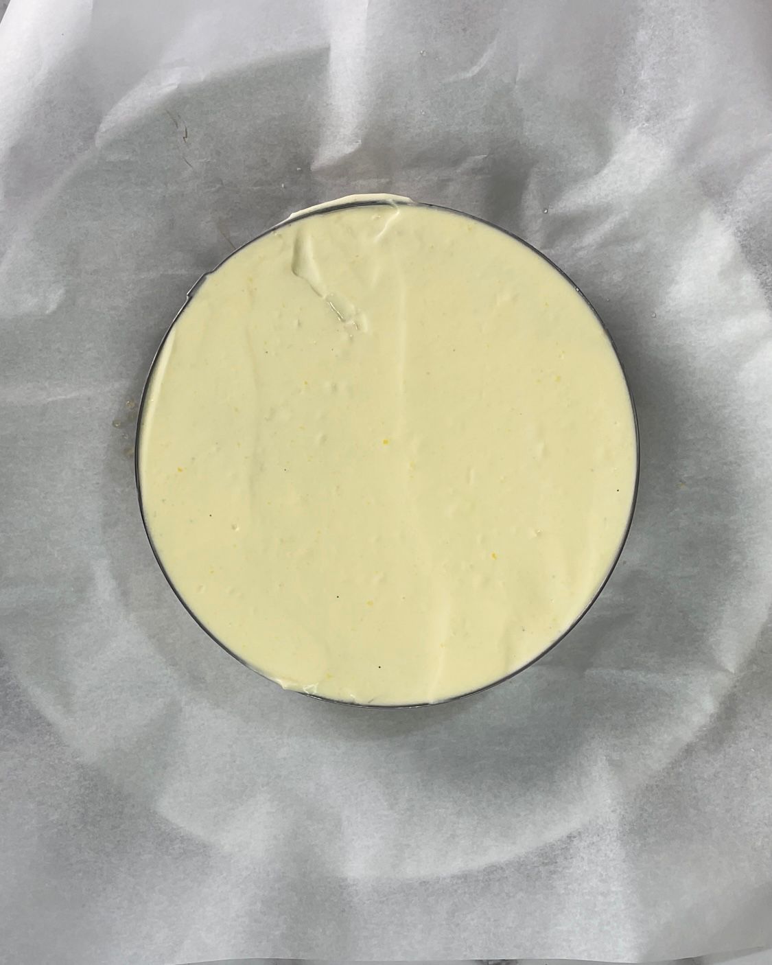 Un cerchio di cheesecake è appoggiato su un pezzo di carta oleata.