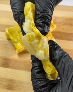 Una persona che indossa guanti neri tiene in mano un pezzo di cibo su un tagliere.