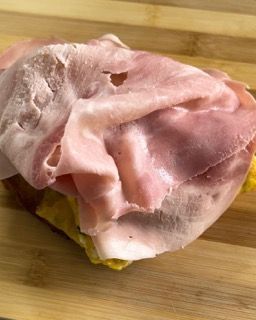 Un pezzo di prosciutto è appoggiato su un tagliere di legno.