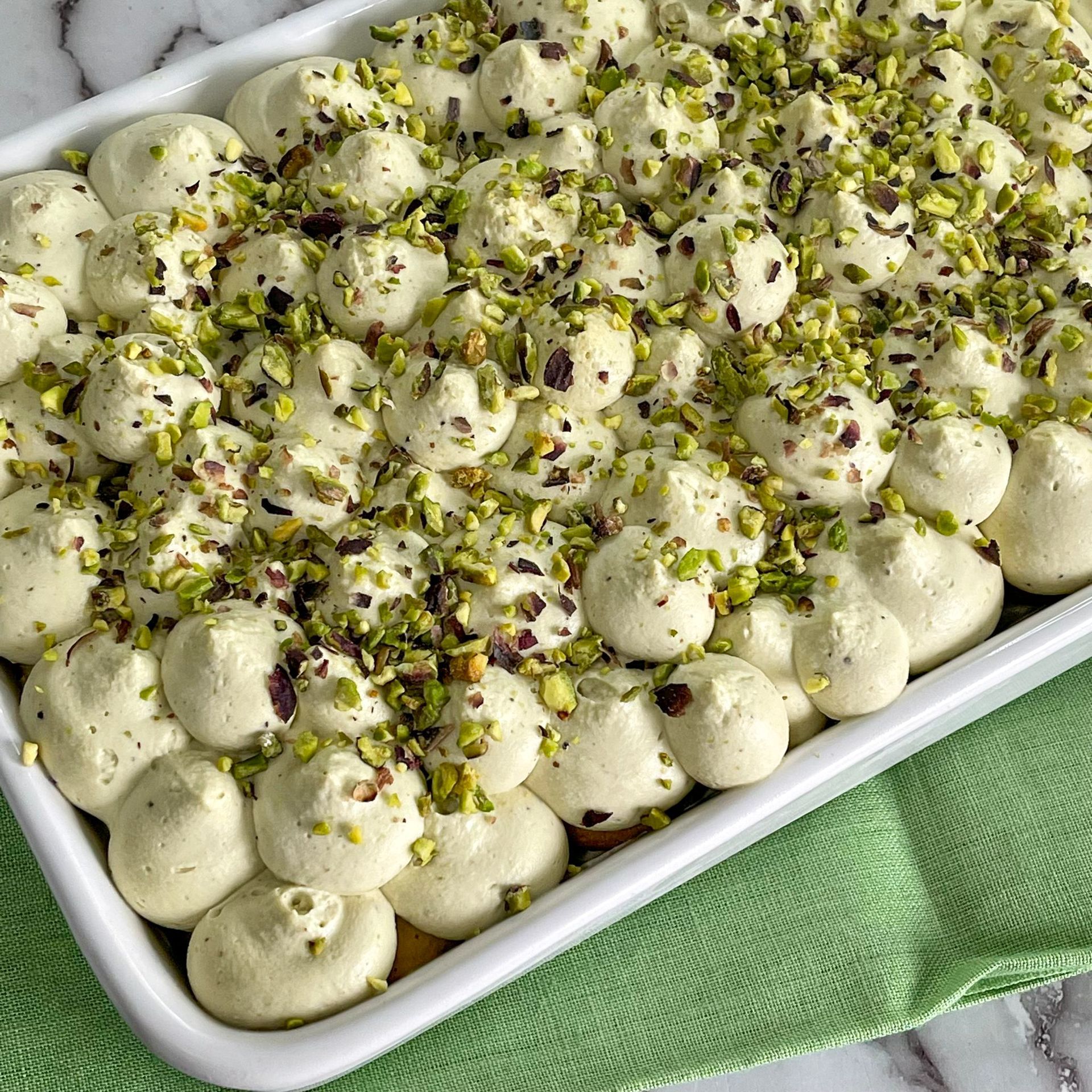 Una teglia bianca ripiena di panna montata e pistacchi.