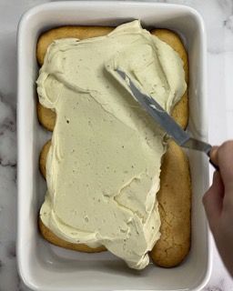 Una persona sta spalmando la glassa su una torta in una teglia.