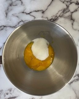 Una ciotola di metallo piena di uova e yogurt su una superficie di marmo.