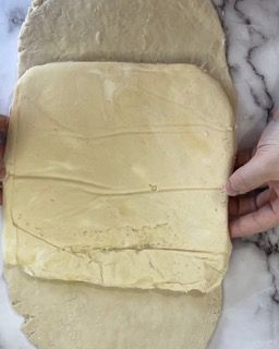 Una persona tiene in mano un pezzo di pasta su una superficie di marmo.