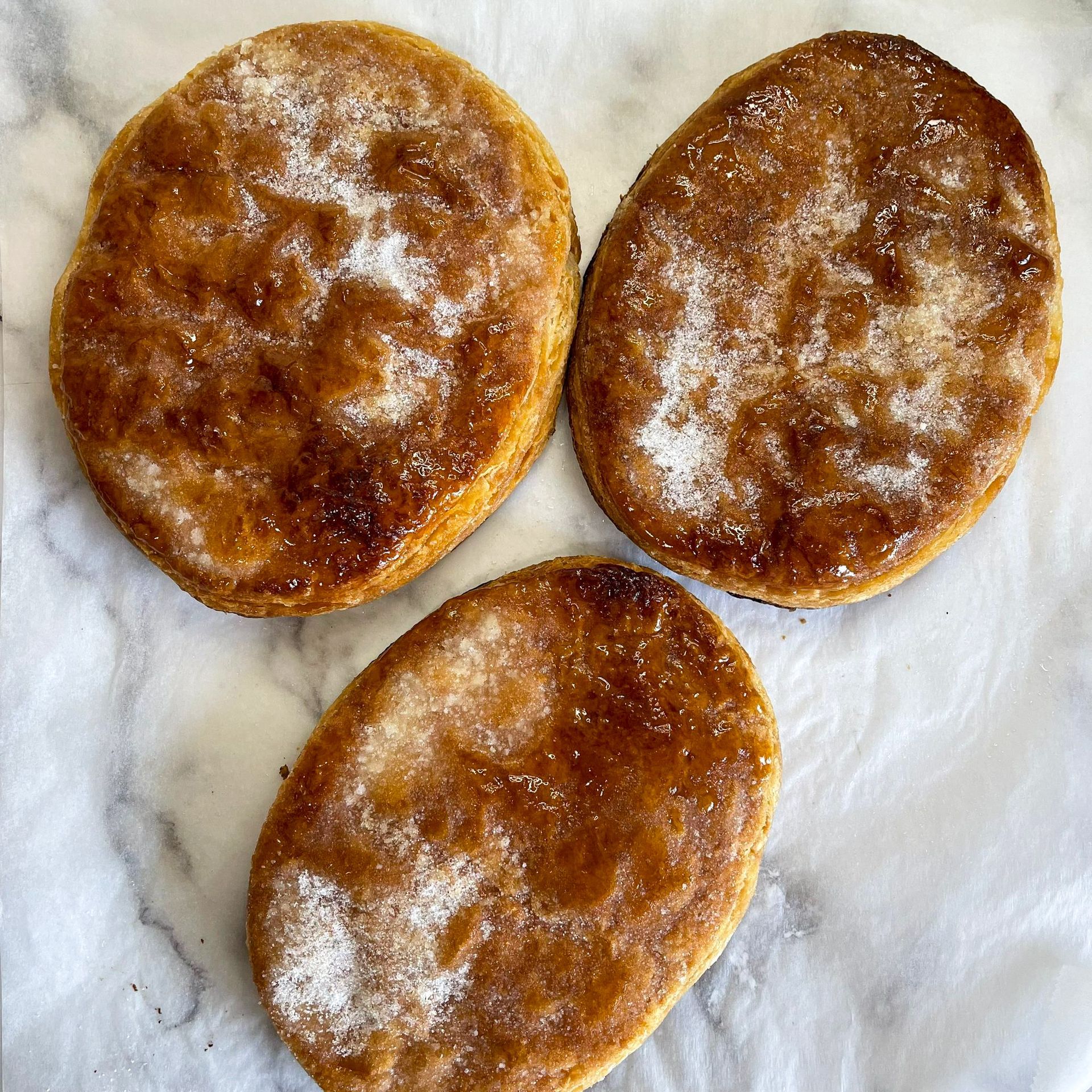 Tre biscotti ricoperti di zucchero a velo sono appoggiati su una superficie di marmo.
