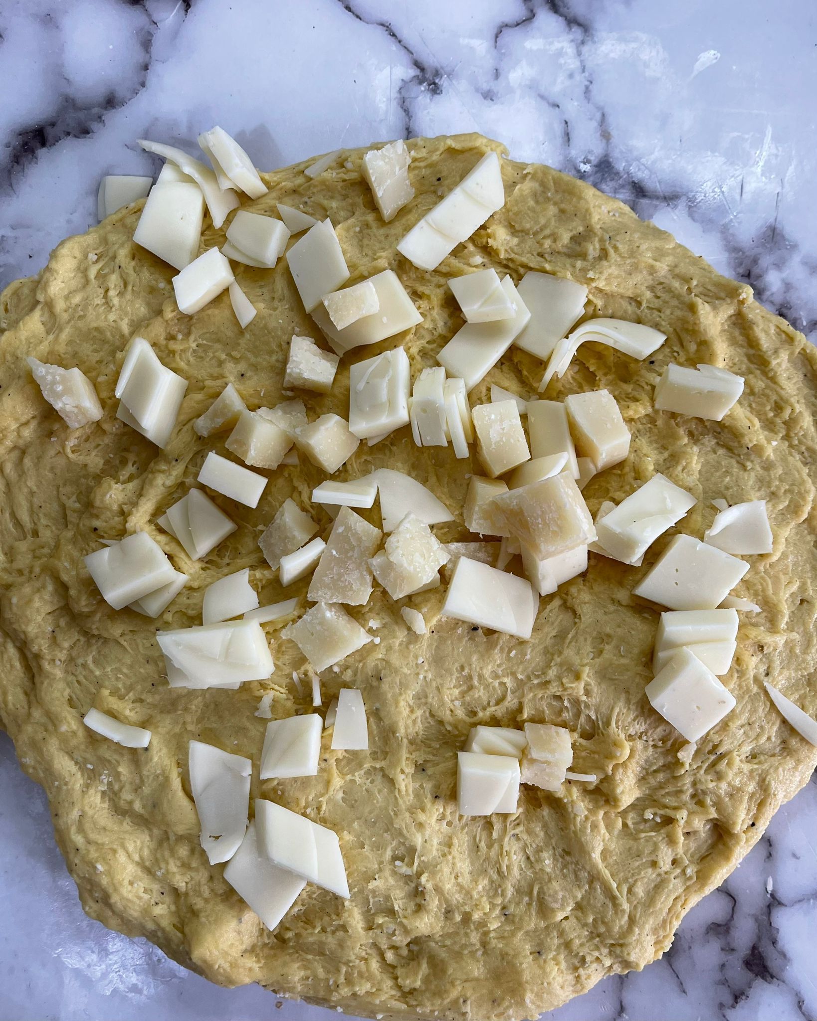Un impasto per pizza con formaggio tritato sopra, su una superficie di marmo.