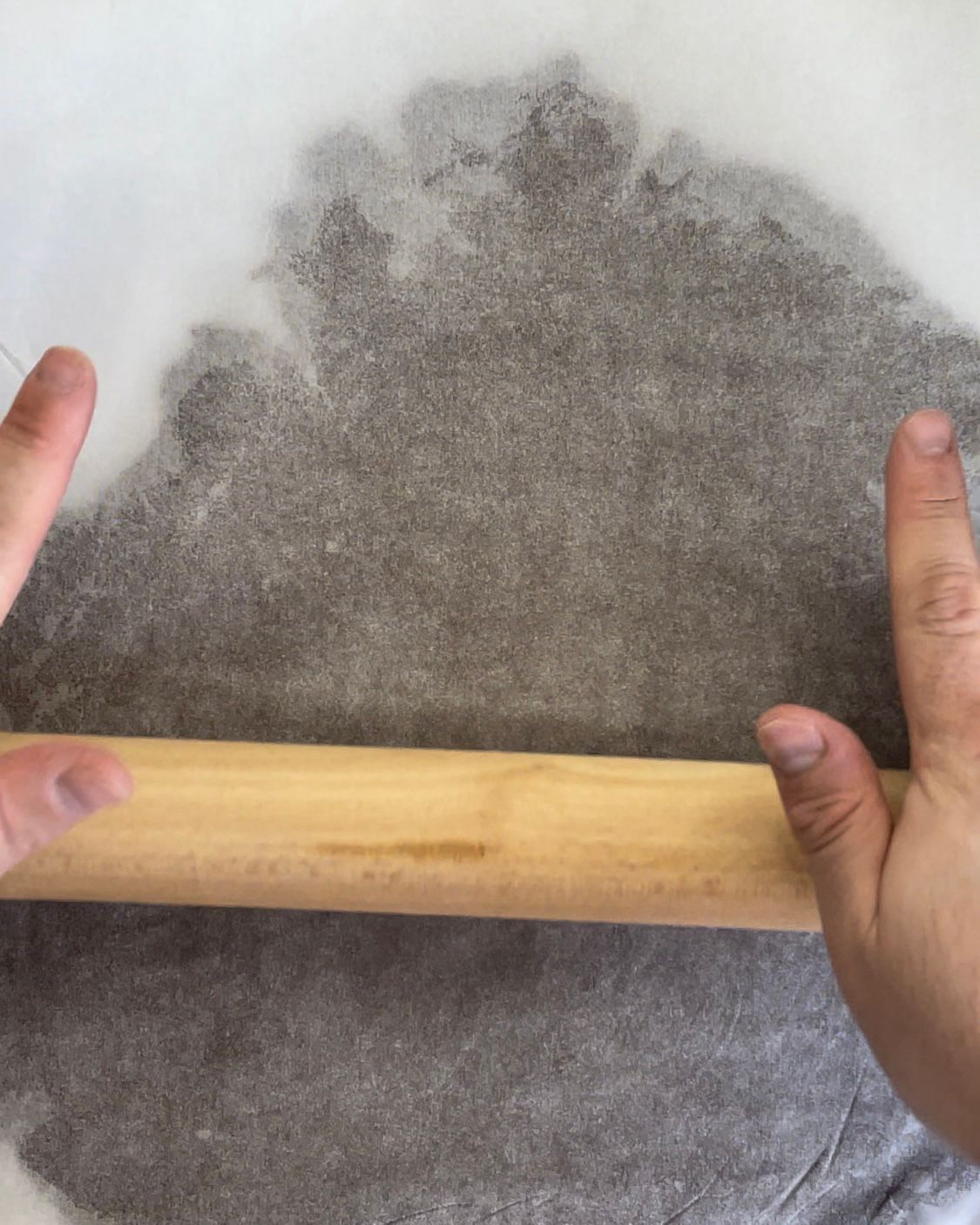 Una persona sta stendendo la pasta con un mattarello di legno.