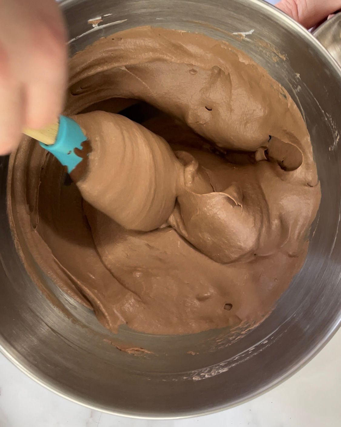 Una persona sta mescolando la glassa al cioccolato in una ciotola di metallo con una spatola.
