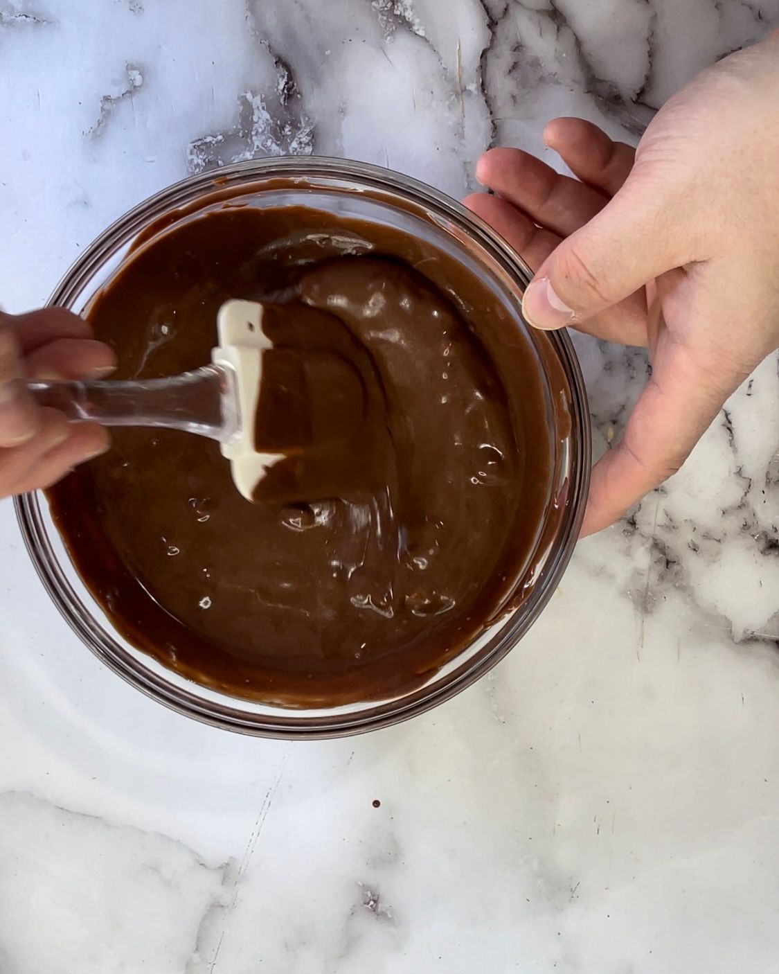 Una persona sta mescolando una ciotola di salsa al cioccolato con una spatola.