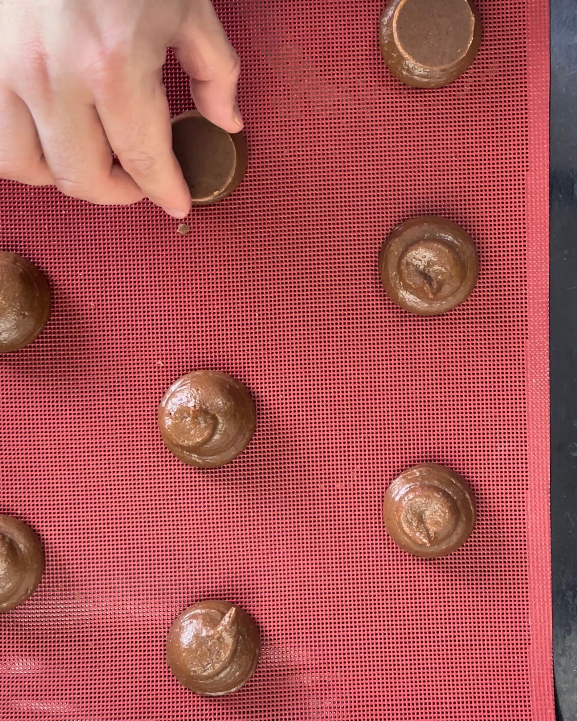 Una persona sta mettendo dei biscotti al cioccolato su un tappetino rosso.