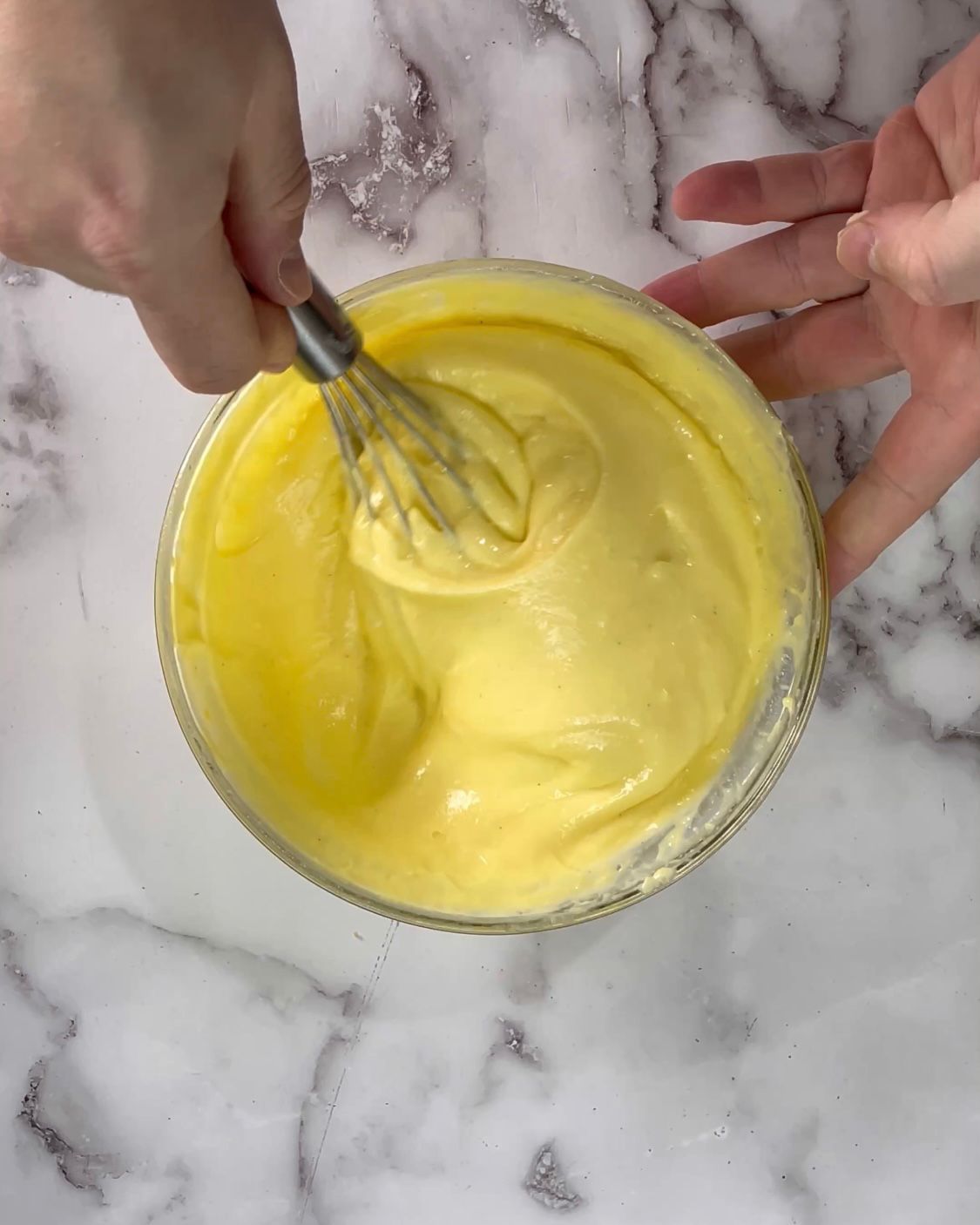 Una persona sta mescolando un liquido giallo in una ciotola con una frusta.