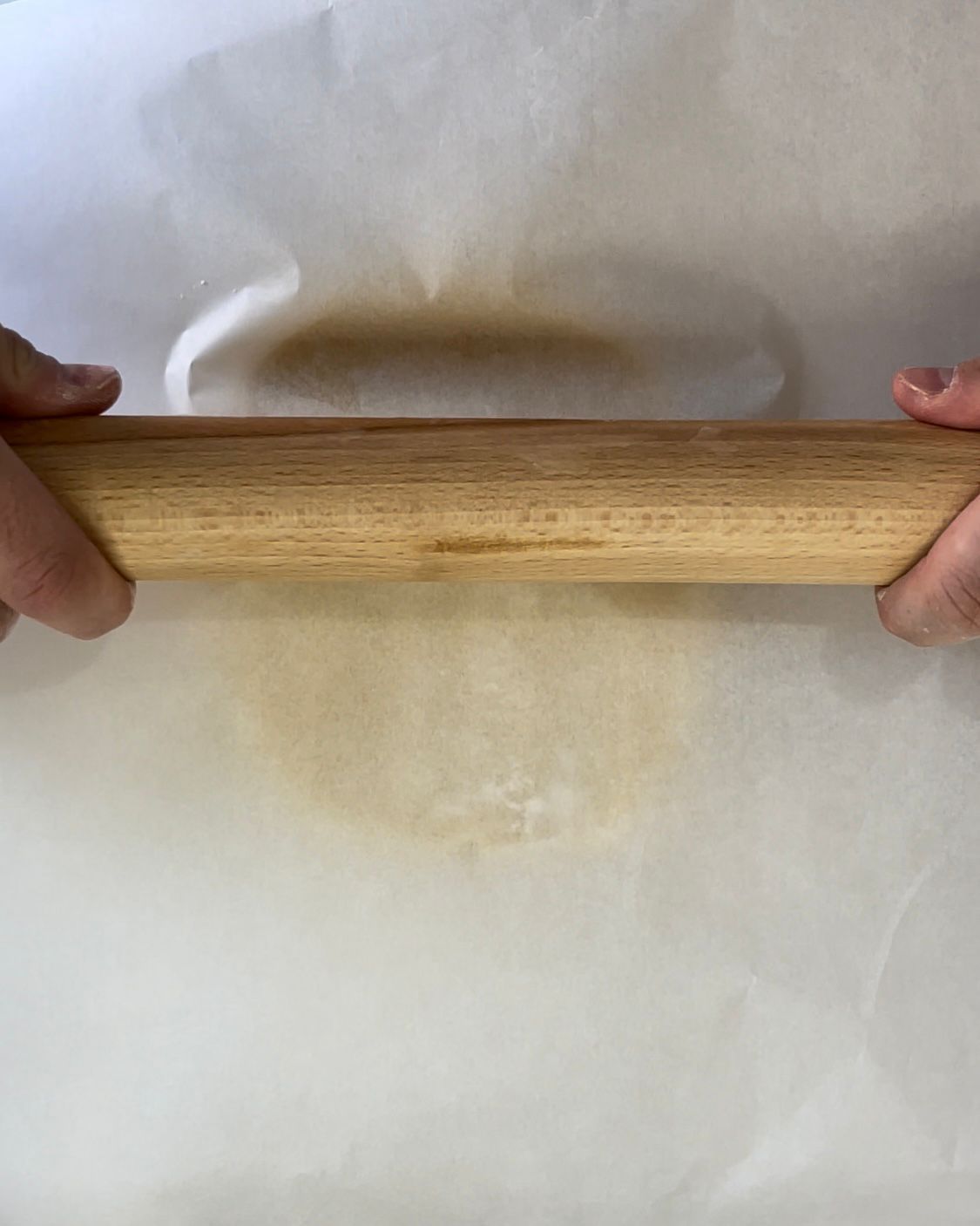 Una persona sta stendendo la pasta con un mattarello di legno su un pezzo di carta oleata.
