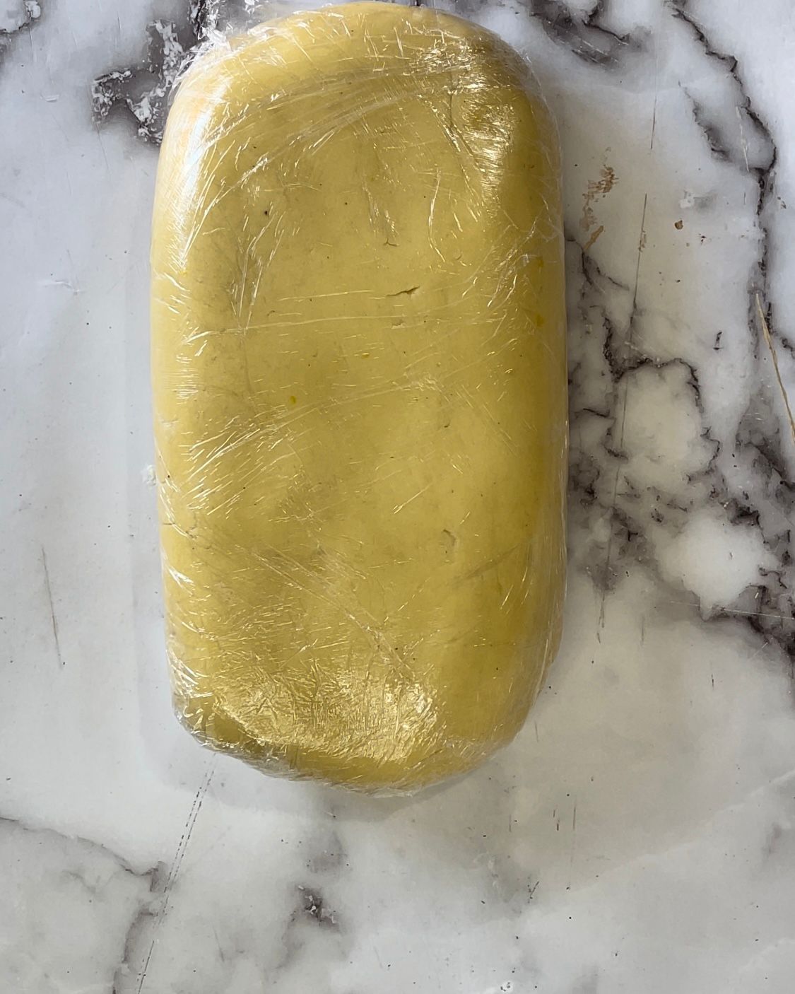 Un pezzo di impasto è avvolto in pellicola trasparente su una superficie di marmo.