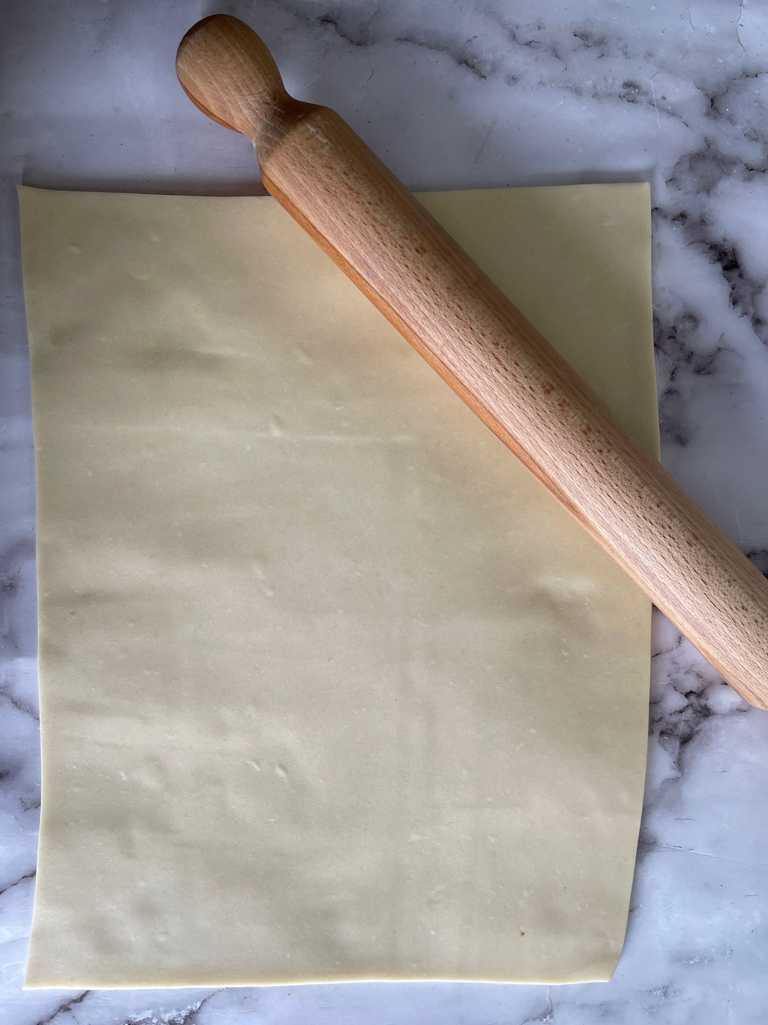 Un mattarello di legno è appoggiato su un pezzo di pasta.