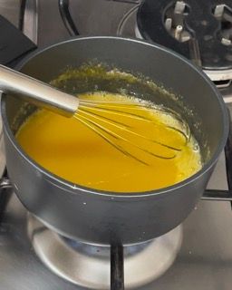 Una pentola piena di liquido giallo con una frusta dentro, su un fornello.