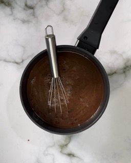 Una pentola di salsa al cioccolato con dentro una frusta.