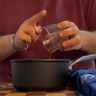 Una persona che versa del liquido in una pentola da una tazza graduata
