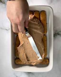 Una persona sta spalmando la glassa al cioccolato su una teglia di biscotti.