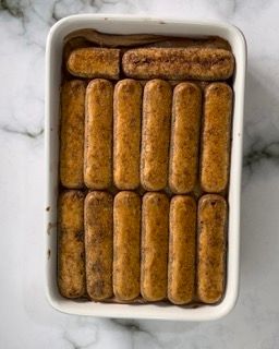 Una casseruola bianca piena di bastoncini di salsiccia su un tavolo.